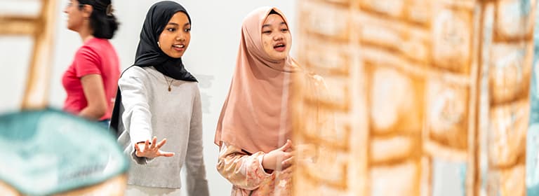 Two female students in hijabs commenting on an art exhibit in a gallery