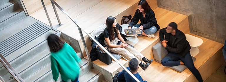 Four students talking happily on a seating area beside a stairway