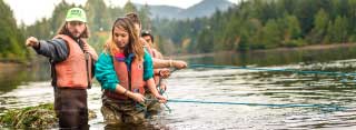 Researchers in life jackets stand hip-deep in the ocean pulling on a net.