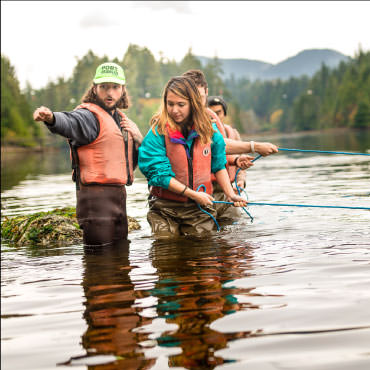 People with red life jackets pulling blue ropes in water