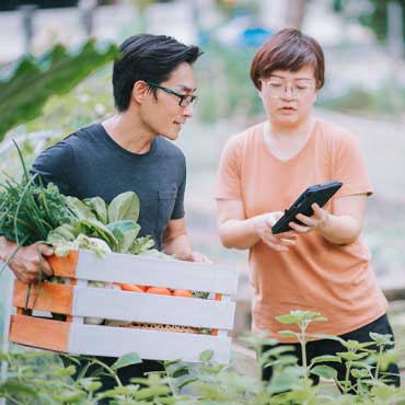 Two farmers – one carrying a box of vegetables and the other one holding a tablet.
