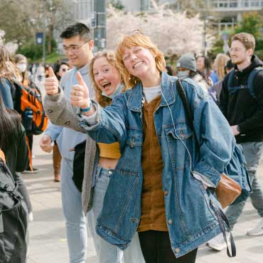Two UBC students in a crowd on campus giving thumbs up