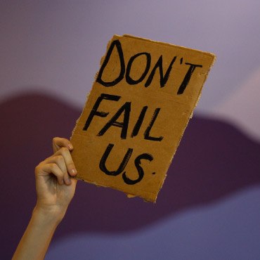 Hand holding up cardboard sign that says "don't fail us"