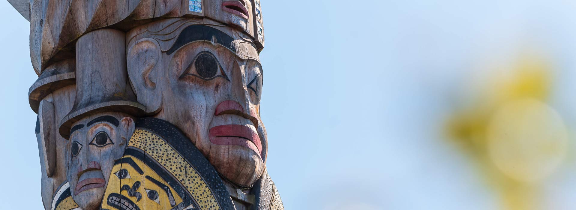 A close-up of a reconciliation pole carved with human faces against a clear sky