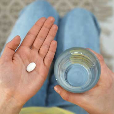 Person holding a pill in one hand with a glass of water in the other hand.