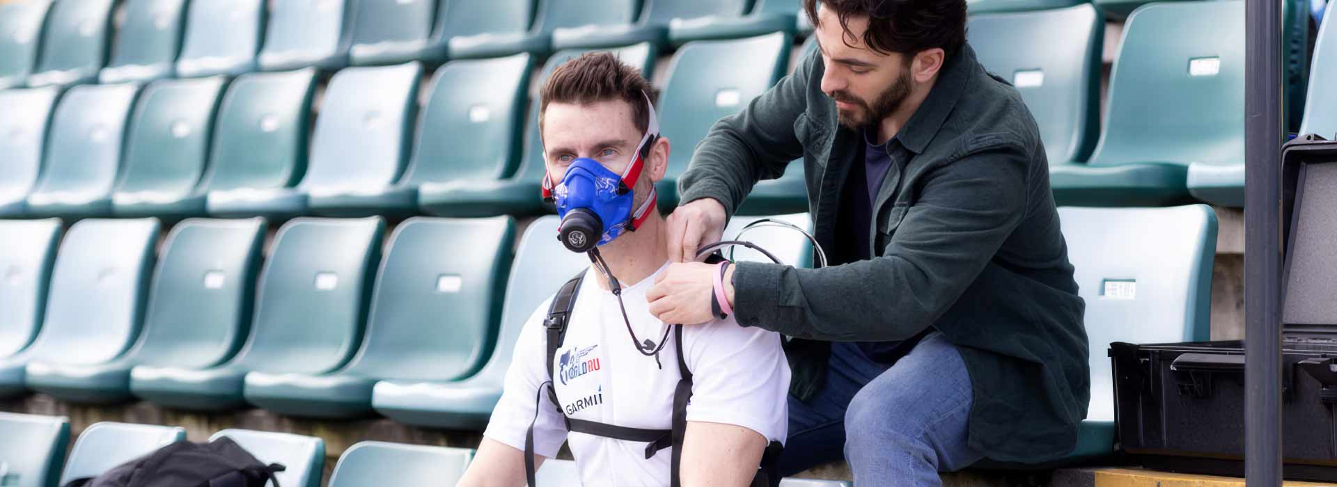 A person assisting another person with an aerobic and heart rate mask, in an outdoor stadium